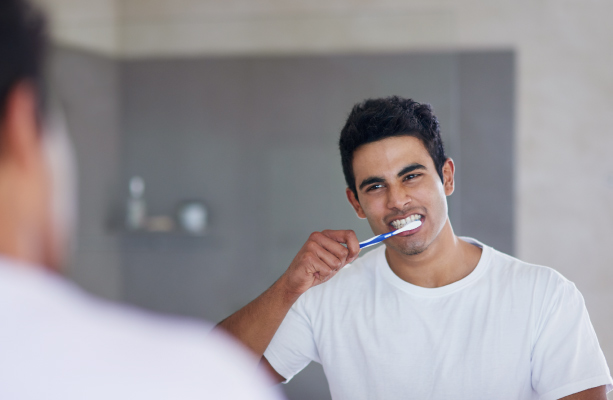 dark haired man standing in front of mirror brushing teeth with fluoride toothpaste to help teeth