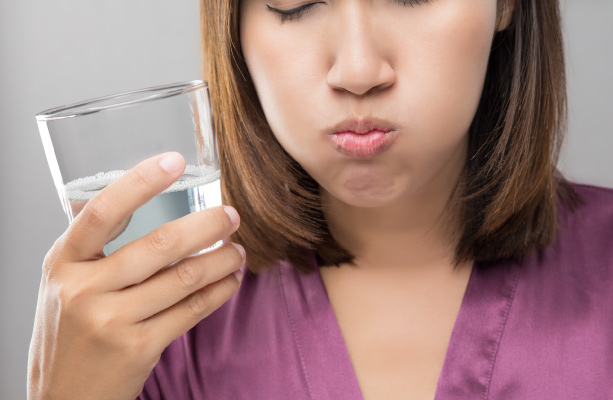 Young brunette woman in purple shirt holding a small glass with clear liquid and rinsing mouth out