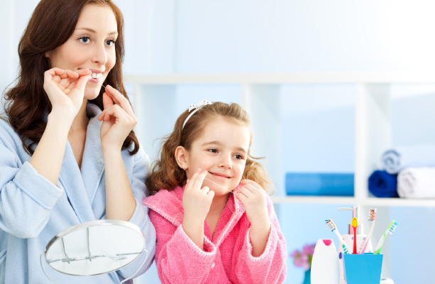 A mother and daughter in colorful bathrobes flossing their teeth together