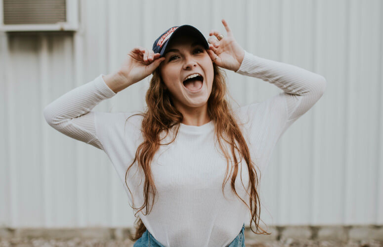 Brunette young woman wears a hat and white shirt as she excitedly shows off her clean tongue