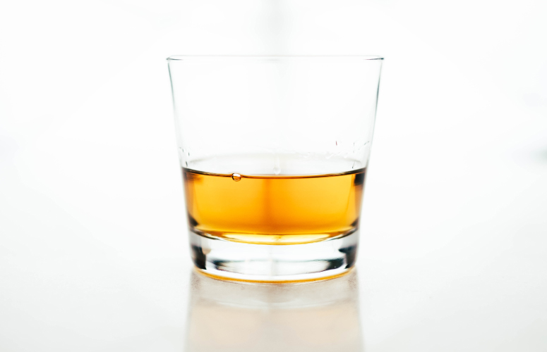 Clear glass of yellow-orange alcohol that will dissolve your teeth's enamel over time