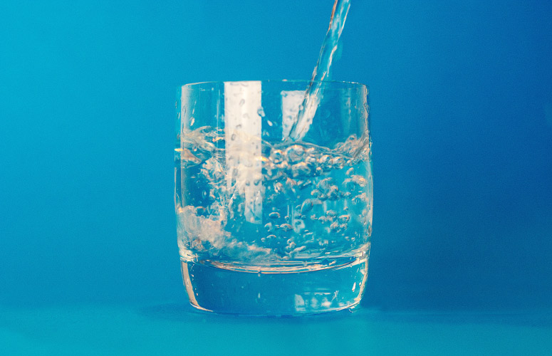 Clear glass against a sky blue background having water poured into it as a healthy alternative to alcohol-based mouthwash