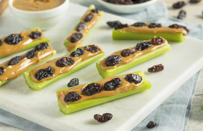 Ants on a log made with cut celery with peanut butter spread in the grooves topped with raisins