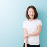 Brunette woman with dental veneers in Canton, GA, smiles while wearing a white shirt against a blue wall