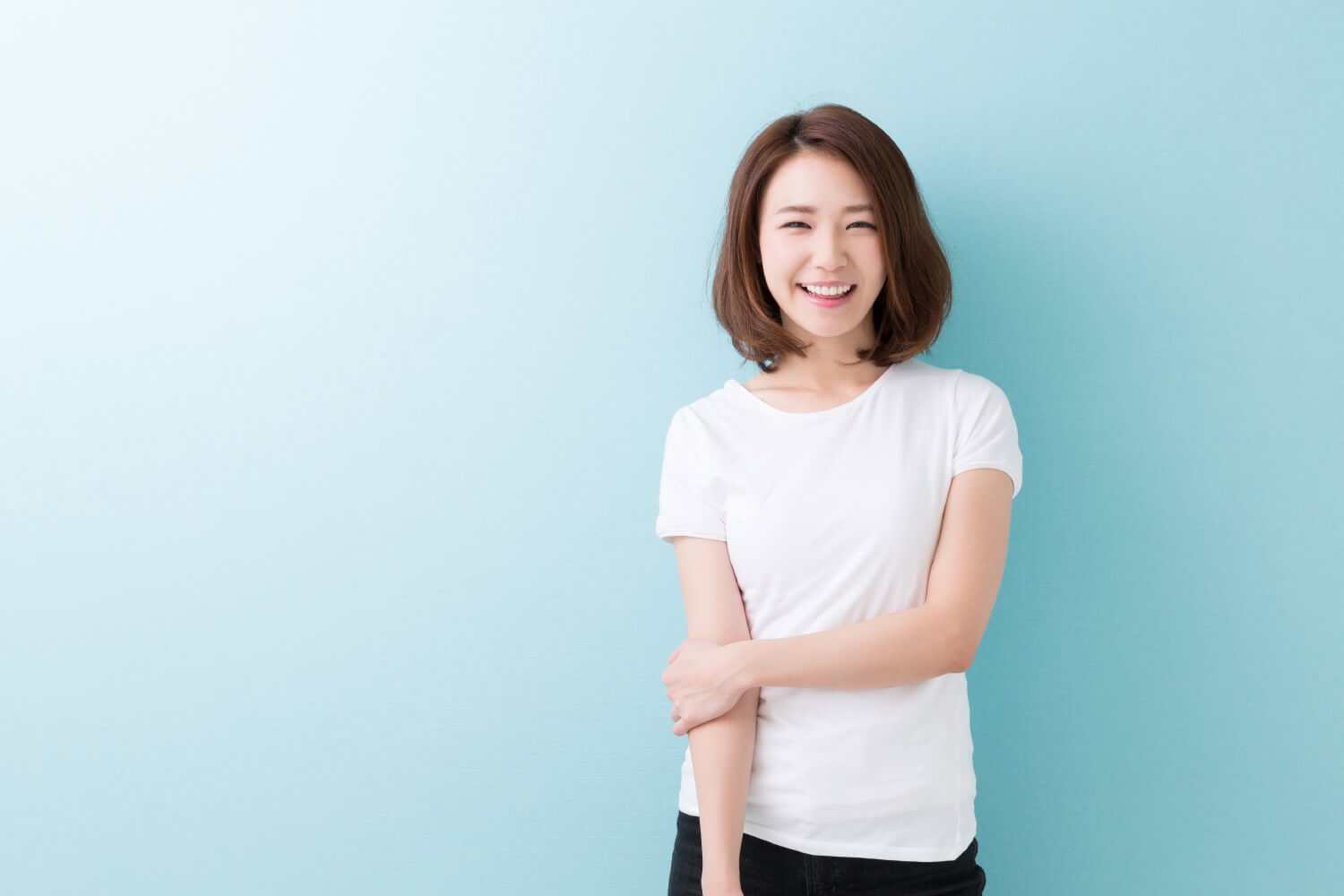 Brunette woman with dental veneers in Canton, GA, smiles while wearing a white shirt against a blue wall