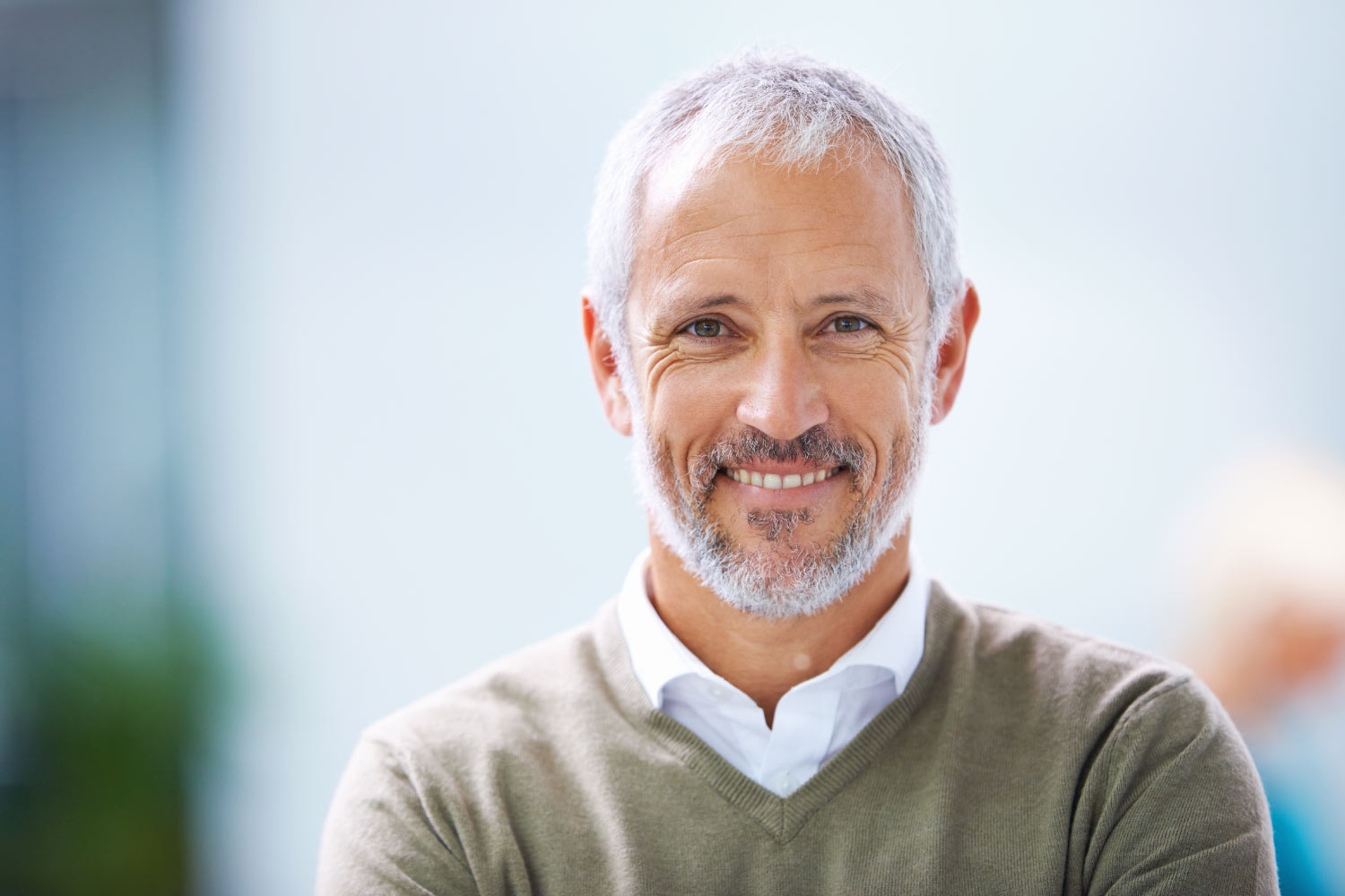 Gray-haired man with dentures smiles while wearing a green sweater