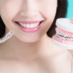 Woman holds Invisalign aligners and braces to compare the two orthodontic treatments