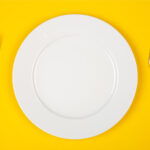 Aerial view of a white plate, fork, and knife on a yellow table for food