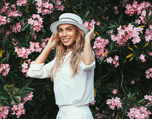 woman in hat smiling in front of flowers