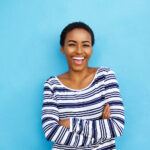 Black woman in a striped shirt smiles against a blue background after tooth bonding