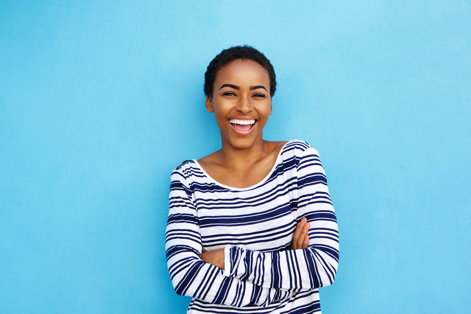 Black woman in a striped shirt smiles against a blue background after tooth bonding