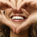 Closeup of a woman holding her hands in a heart shape around her beautiful smile with healthy gums