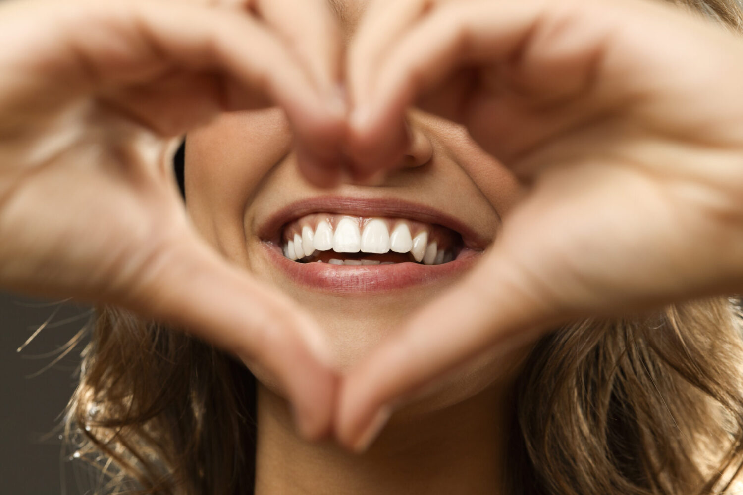 Closeup of a woman holding her hands in a heart shape around her beautiful smile with healthy gums