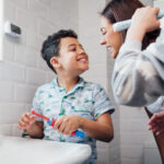 Young boy smiles at his mom after brushing his teeth at their bathroom sink