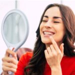 young woman looks in a handheld mirror at her teeth whitening results