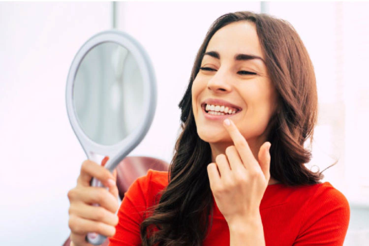 young woman looks in a handheld mirror at her teeth whitening results