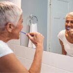 senior woman brushes her teeth to protect her dental restorations